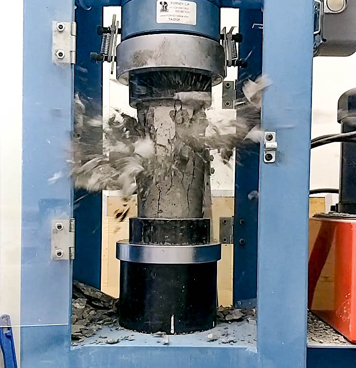 A picture of a cylindrical concrete specimen being tested for compressive strength