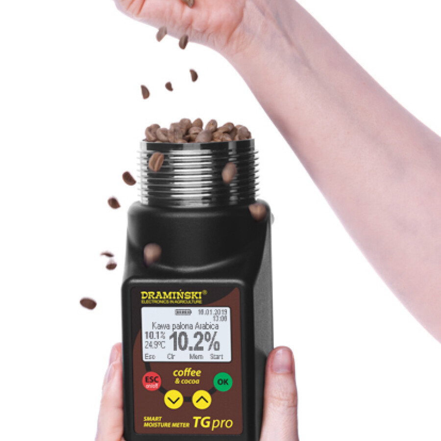 A person holding a moisture meter and a cup of green coffee